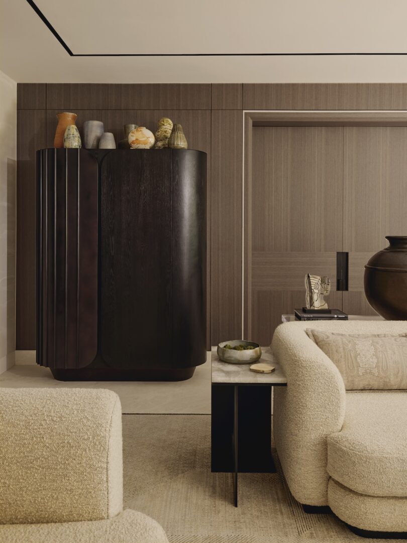 A modern living room with a curved beige sofa, neutral-toned walls, and minimalist wooden cabinetry.