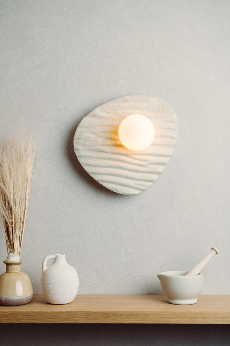 Close-up of a wall light with an oval wooden backplate featuring carved sand-ripple textures.