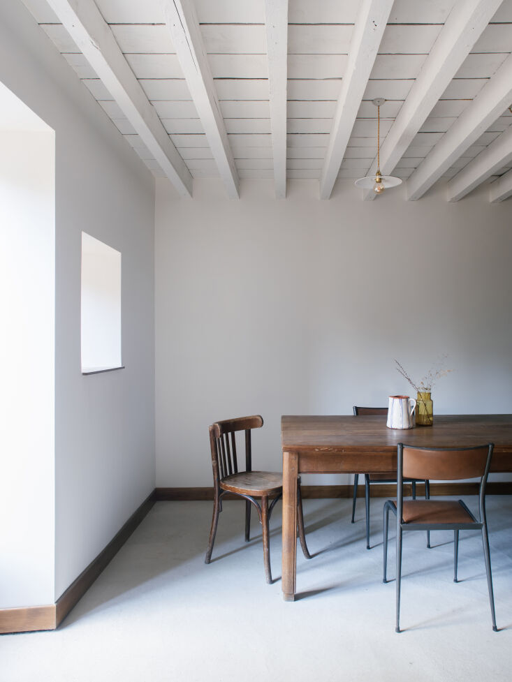Dining area featuring a large stone wall opening, sanded concrete floors, and vintage pendant lighting.