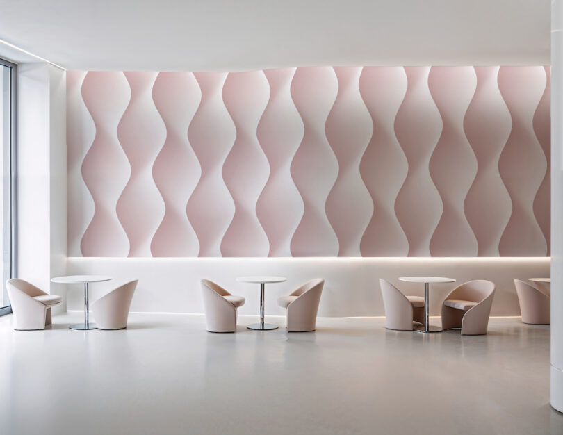 A bright seating area with pink chairs and a soft pink and white wavy patterned wallpaper.