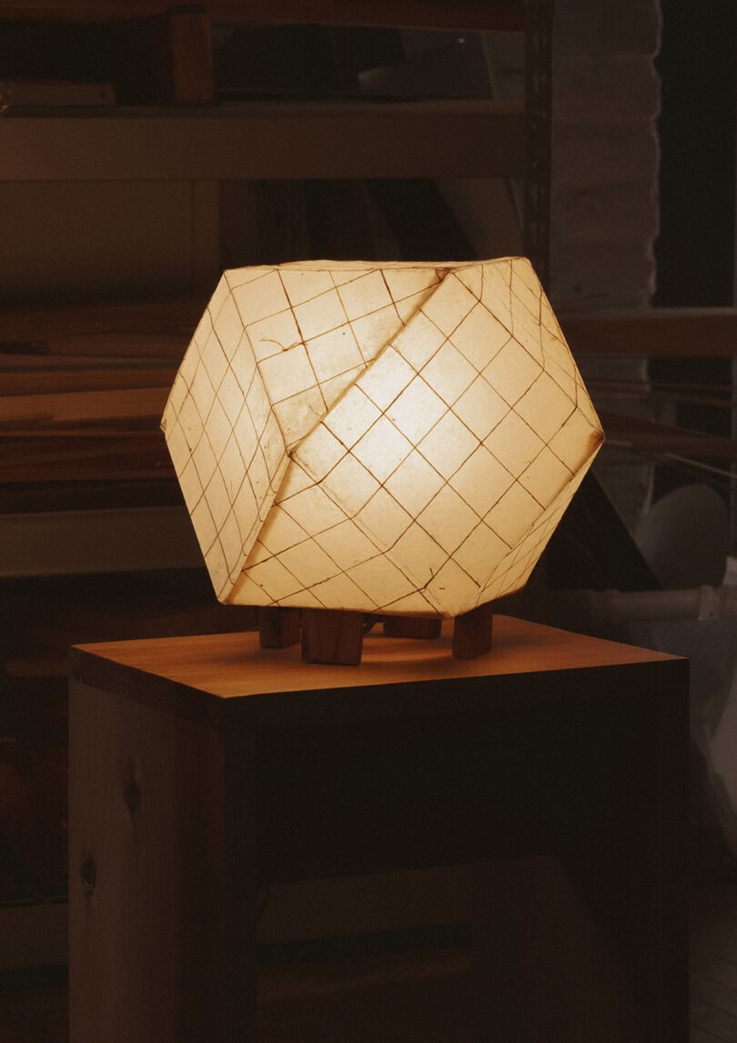 Close-up of a grid-patterned paper lamp emitting a warm, soft glow on a wooden surface.