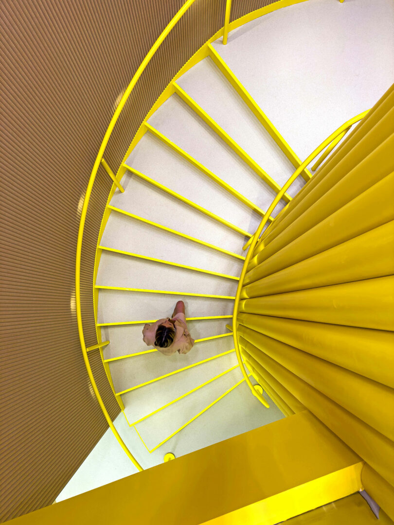 High-angle view of a bright yellow spiral staircase inside the modern office.