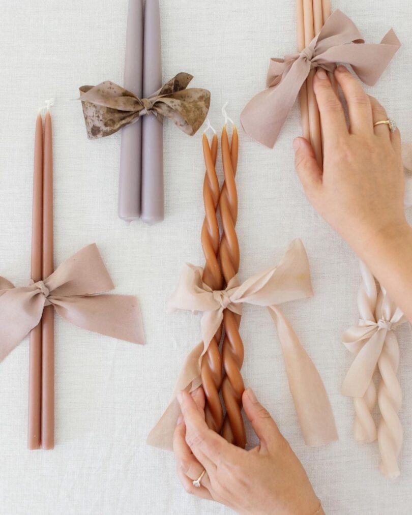 Hands organizing a vibrant collection of colorful twisted candles tied with ribbons.