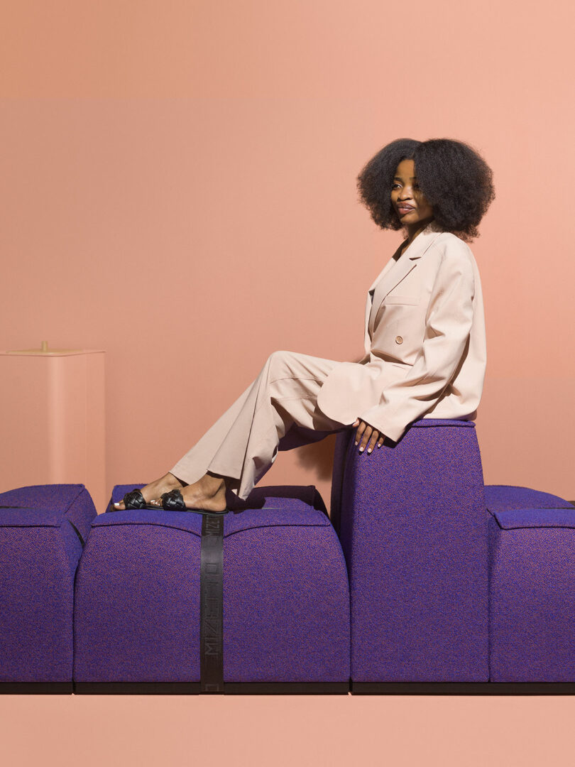 A woman in a beige suit sitting on a purple blocky modular sofa unit.