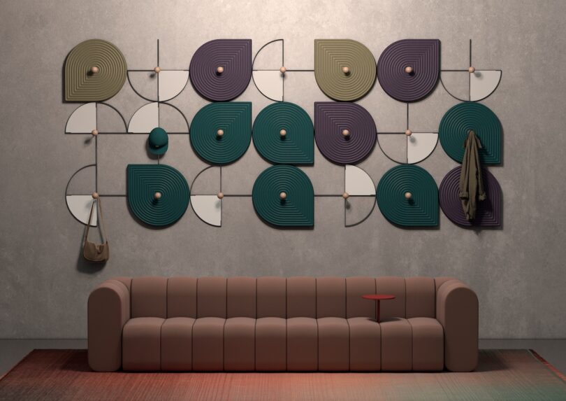 Mauve sofa with a colorful geometric wall art installation used to hang a coat and bag.