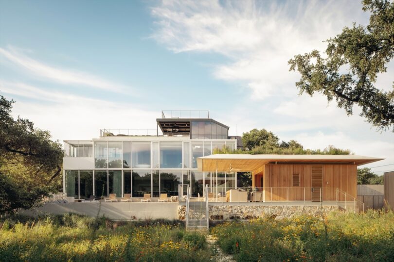 Modern multi-level glass and wood residence set in an open grassy field under a wide Texas sky.