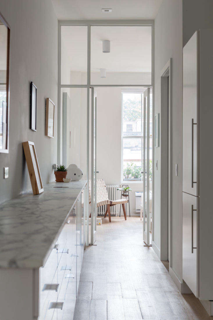 A sleek, narrow Manhattan pass-through kitchen with light wood cabinets and integrated storage solutions.