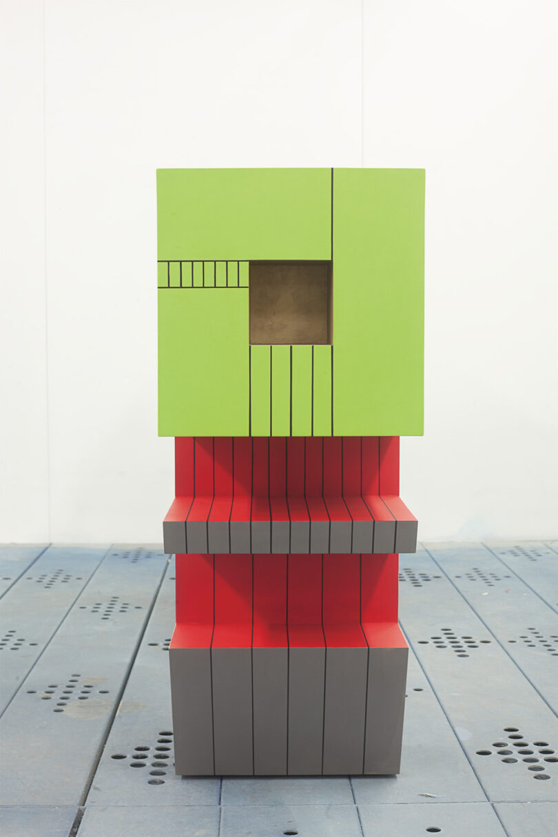 A sculptural piece with stacked green, red, and gray rectangular shapes and linear grooves.