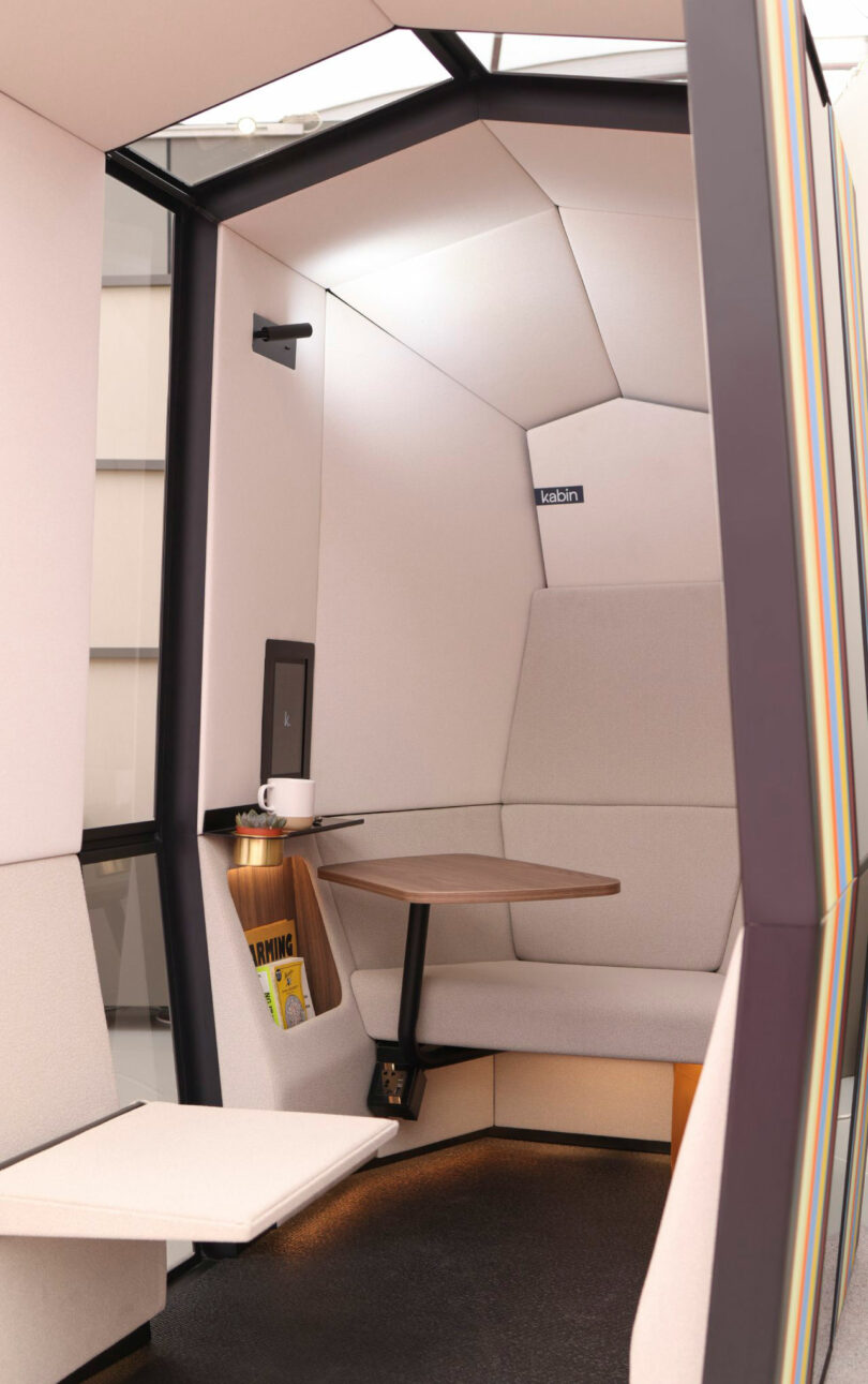 Close-up of a compact work pod interior featuring a wooden table, reading light, and wall-mounted digital screen.