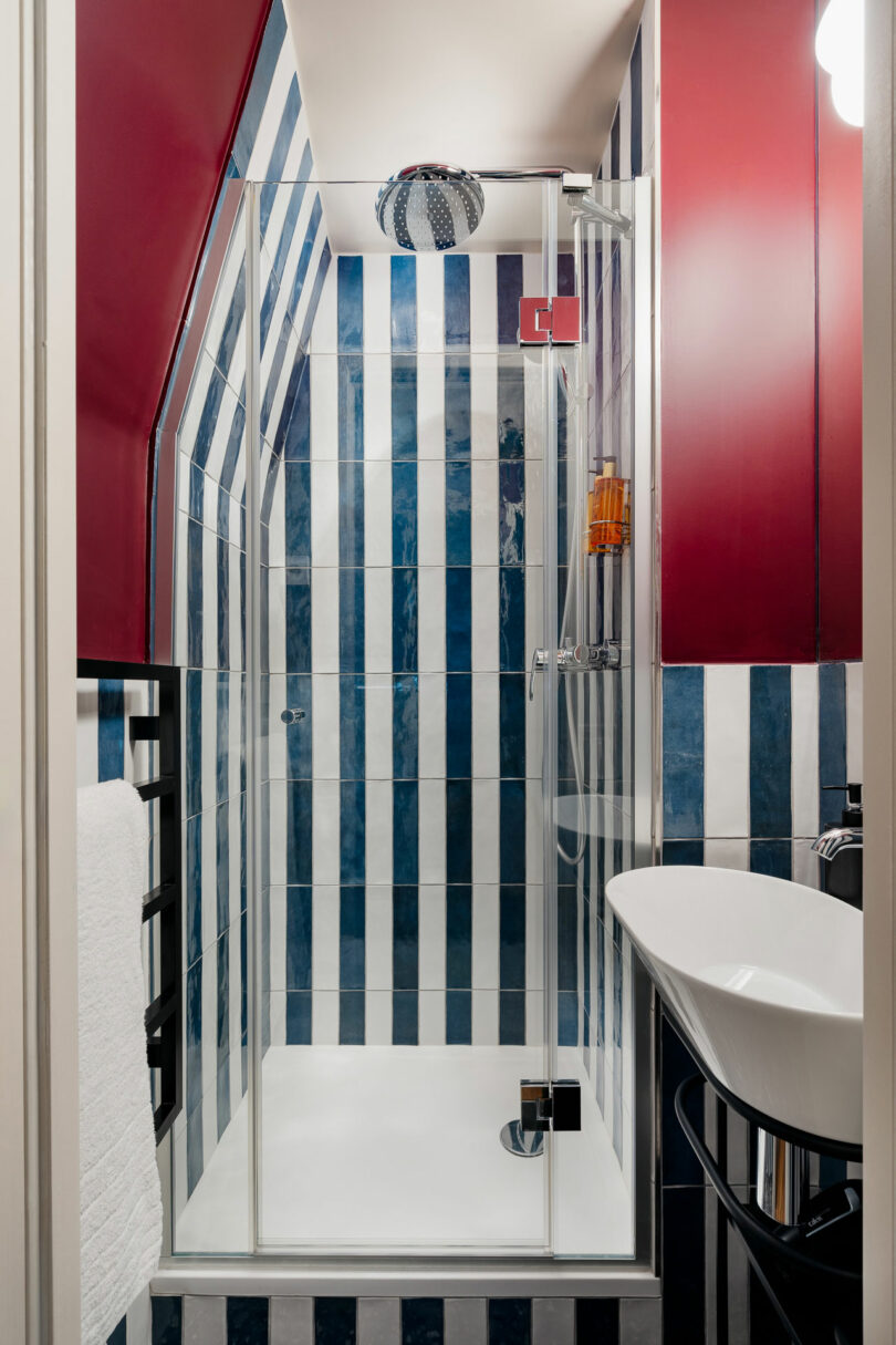 A compact bathroom with vertical blue and white striped tiles and red vanity cabinets.