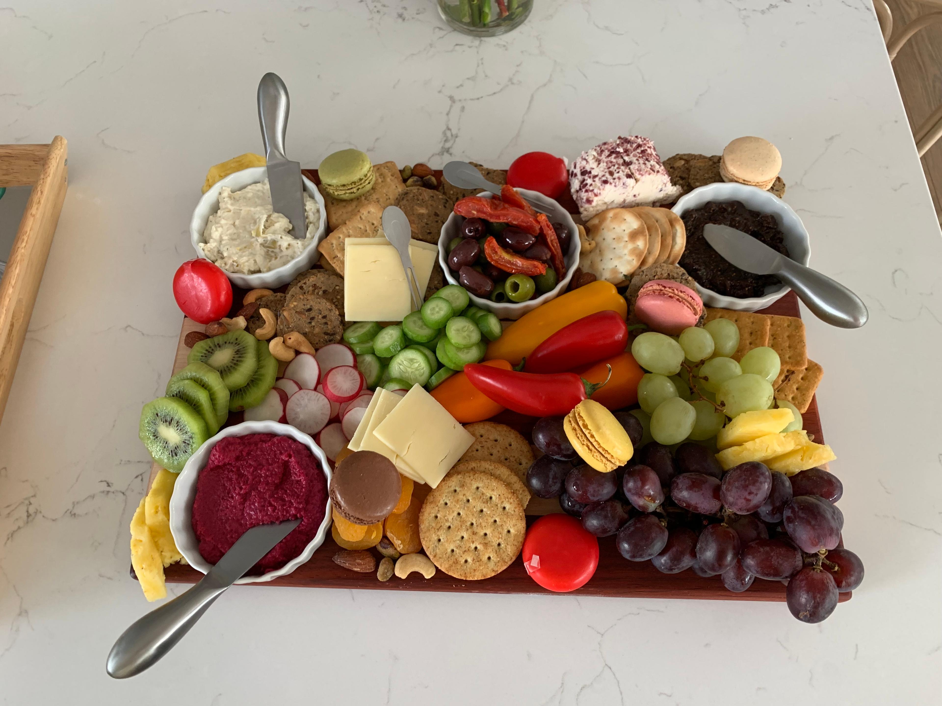 A fully set up charcuterie board showing distinct groups of proteins, starches, and produce.