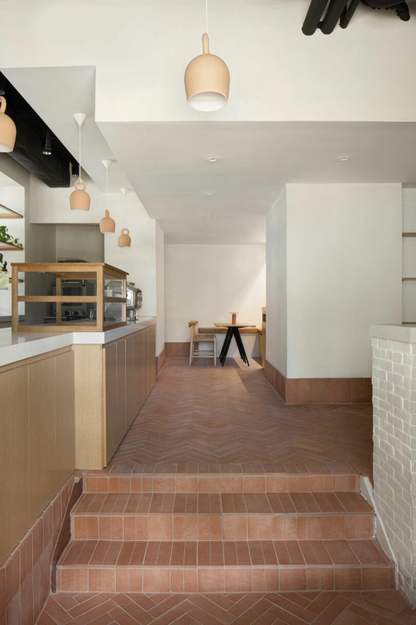 Minimalist cafe interior with terracotta tiles and light wood cabinetry designed by Nicki Gitlin.