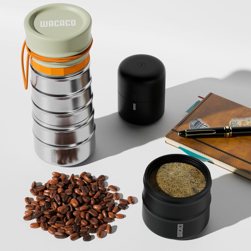 A portable coffee maker, notebook, coffee beans, and a fresh cup of espresso arranged on a white surface.
