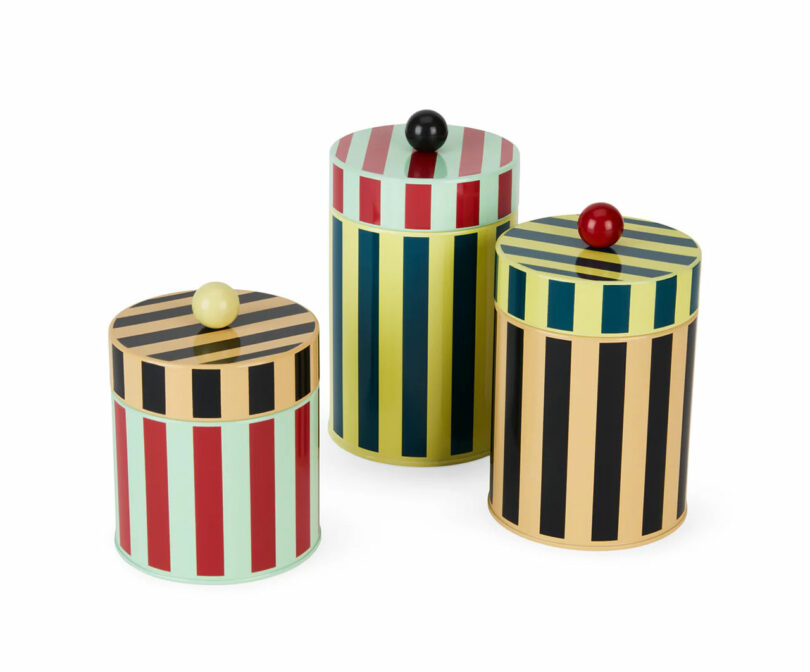Three metal canisters with vibrant vertical stripes and colorful circular lid knobs.