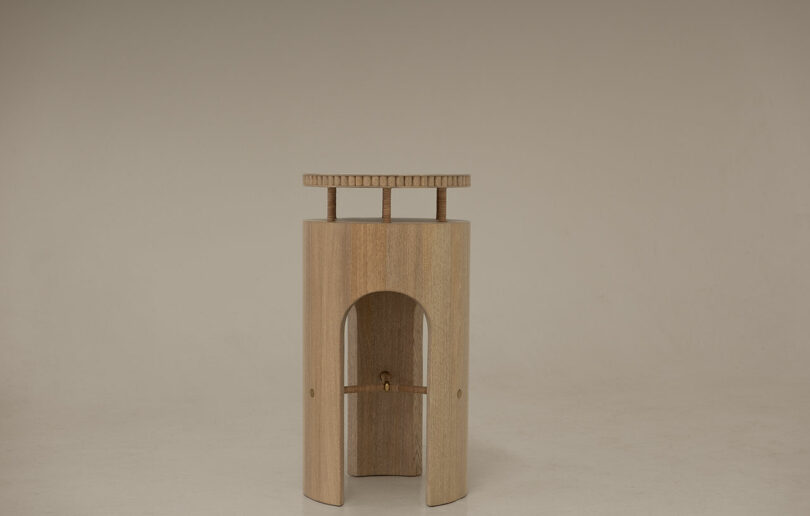 A sculptural wooden object with a central arch and flat rectangular top on a beige background.