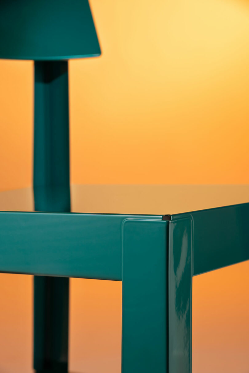 Close-up of a glossy teal metal chair surface reflecting light against an orange background.