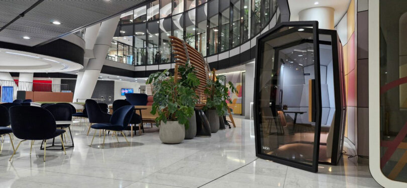 A sleek Kabin glass phone booth positioned on a marble floor in a modern office lobby with lounge seating.