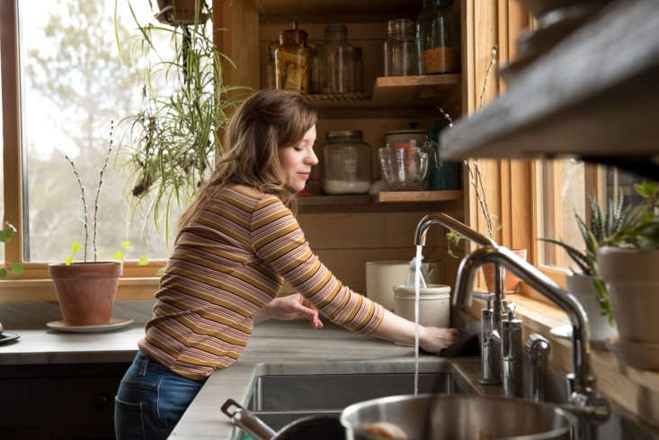 A large stainless steel triple-basin kitchen sink filled with dishes and cleaning tools.