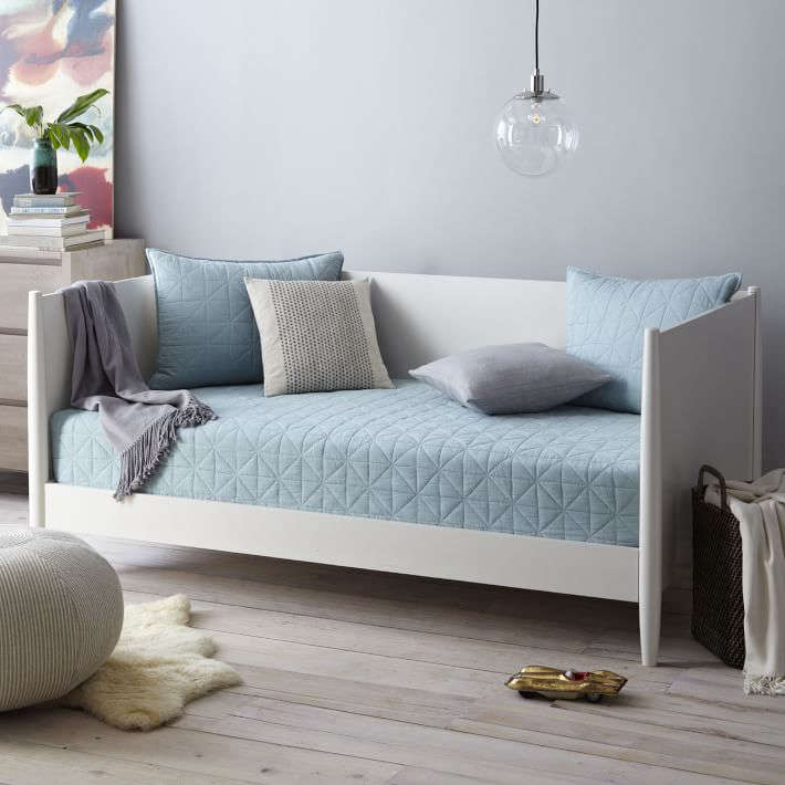 A white upholstered mid-century style daybed with tapered wood legs from West Elm.