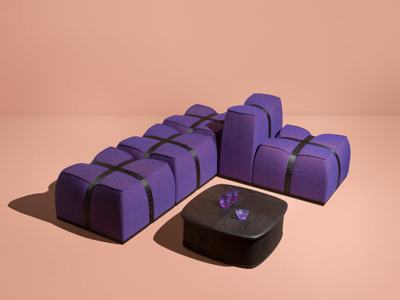 Purple L-shaped modular sofa with black straps next to a low black coffee table.