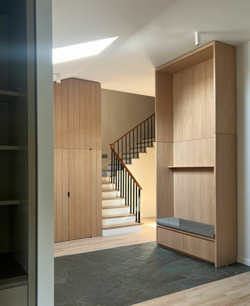 Modern entryway with slate flooring, wooden cabinetry, and a sleek black staircase railing.