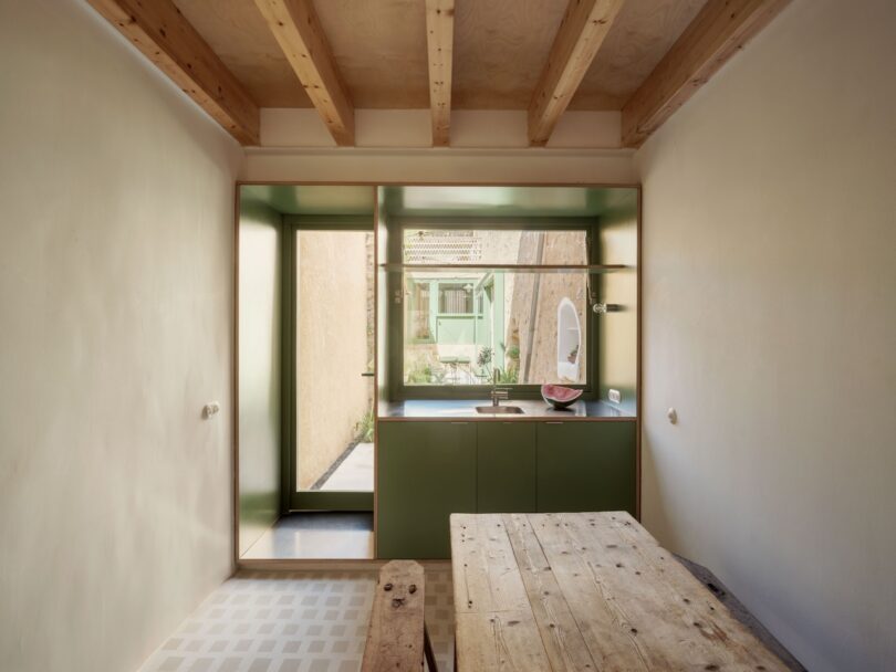 Minimalist kitchen with green cabinets and a wooden table looking out toward the garden.