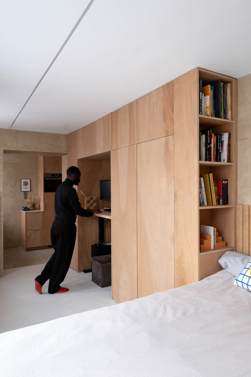 A person working at a built-in wooden desk integrated into floor-to-ceiling cabinetry.