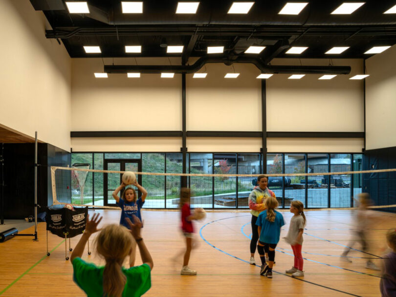 Indoor volleyball game in a spacious modern gym with polished wood floors and high ceilings.