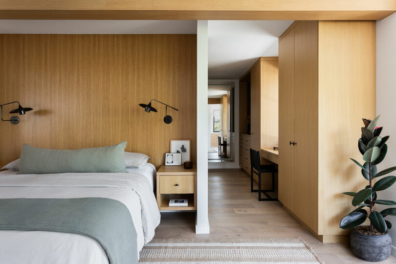 Modern bedroom with wood panel walls, built-in desk, and minimalist decor on light wood flooring.