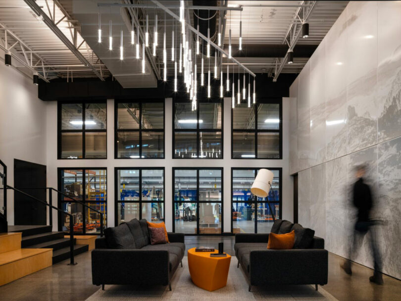 Modern office lobby with dark sofas and views of a workshop through large internal windows.