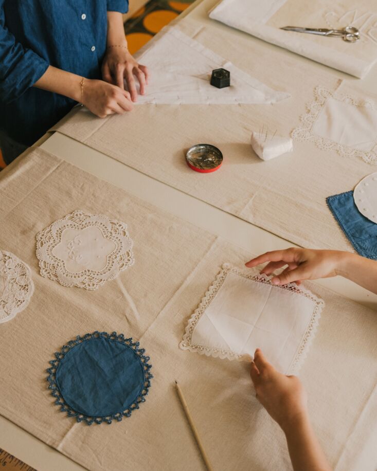 Hands of artisans pinning and preparing lace napkins for embroidery in the Marseille atelier.