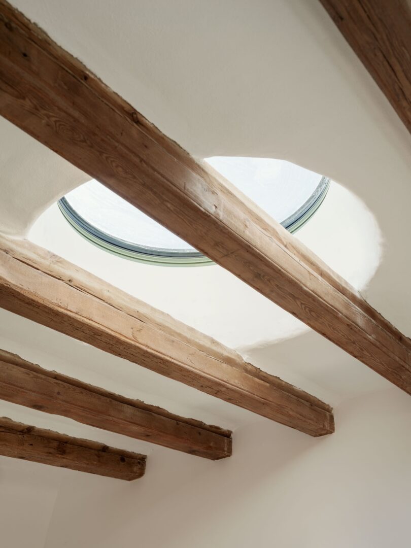 Close-up of a circular skylight set into a white ceiling with exposed wooden beams.
