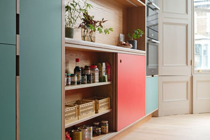 A close-up of shallow pantry shelves containing colorful recycled plastic crates for organization.