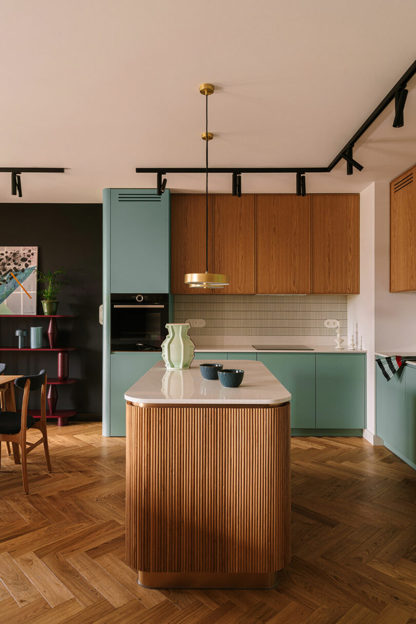 Modern kitchen featuring mint green and light wood cabinets with a marble-topped island and pendant lighting.