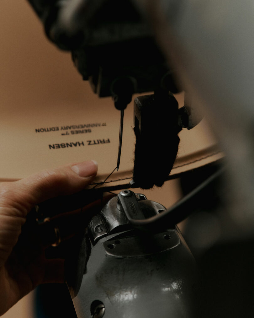A hand guiding material labeled 'FRITZ HANSEN 7 ANNIVERSARY EDITION' through a sewing machine.