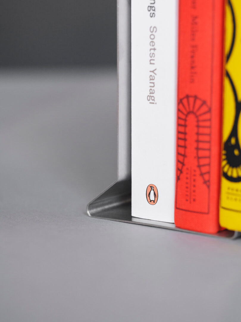 A close-up of a book with the Penguin Books logo on its spine being supported by a metal bookend.