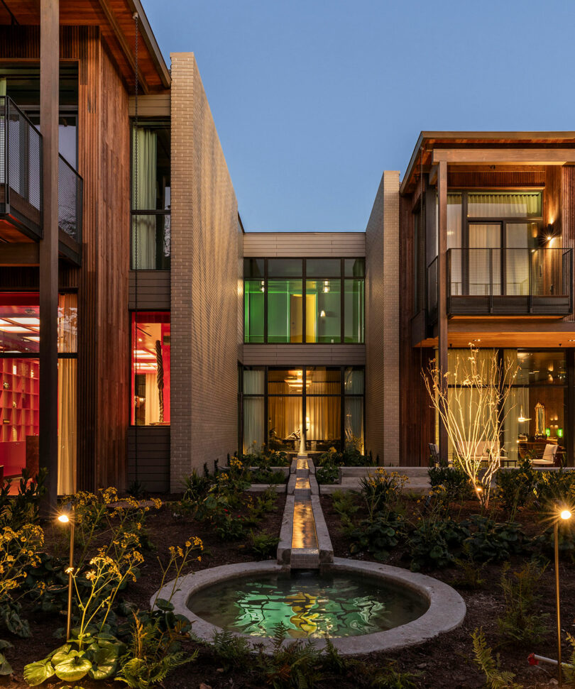Exterior view of the hotel's two-story buildings and courtyard featuring a central water feature at dusk.