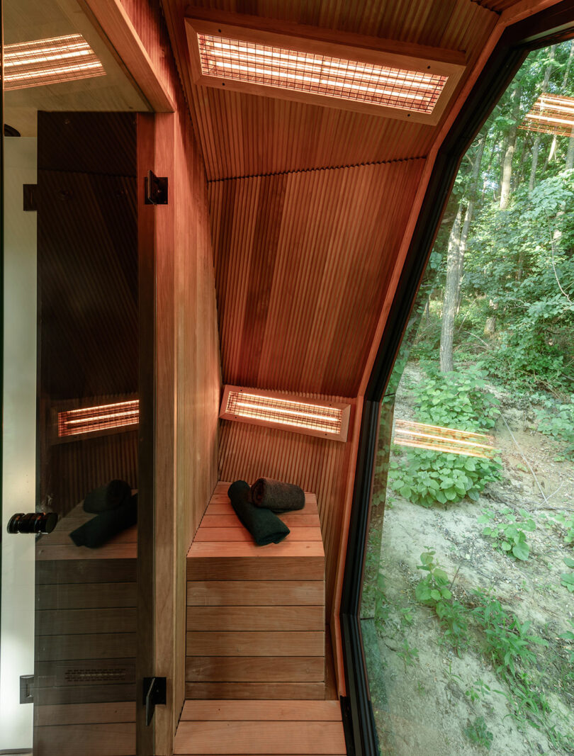 A modern wooden infrared sauna with a large window facing a forest.