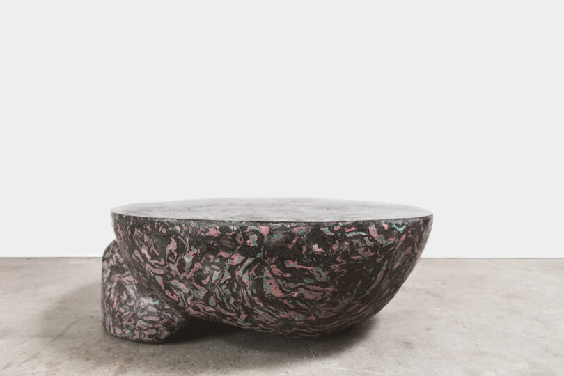 Low, round marbled coffee table with dark surfaces and pink accents in a modern setting.