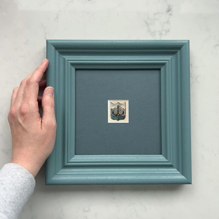 A small antique artwork housed in a frame and mat all painted in the same deep blue shade.