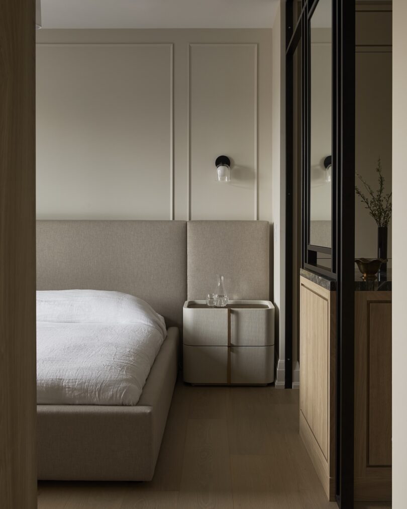 Minimalist bedroom with a beige upholstered bed and a black wall-mounted light.