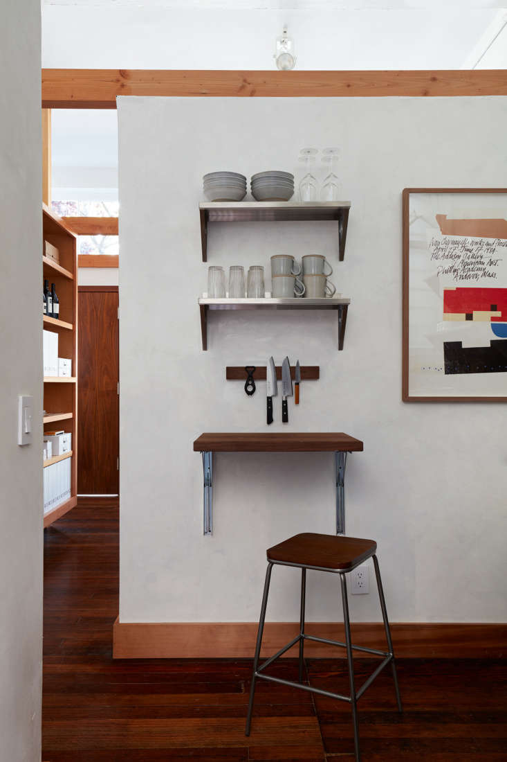 A wall-mounted walnut cutting board used as a secondary counter surface next to a textured lime-plaster wall.