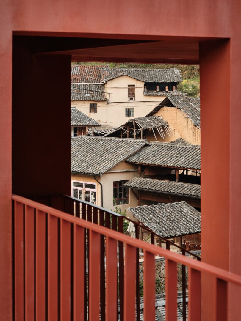View through a red rectangular architectural frame overlooking traditional village houses with tiled roofs.