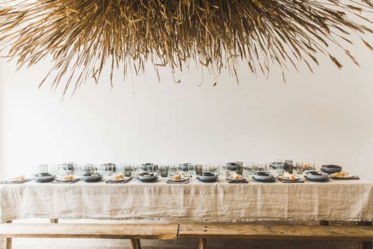 A large, cloud-like installation made of dried reeds and wheat stalks floating above a table.