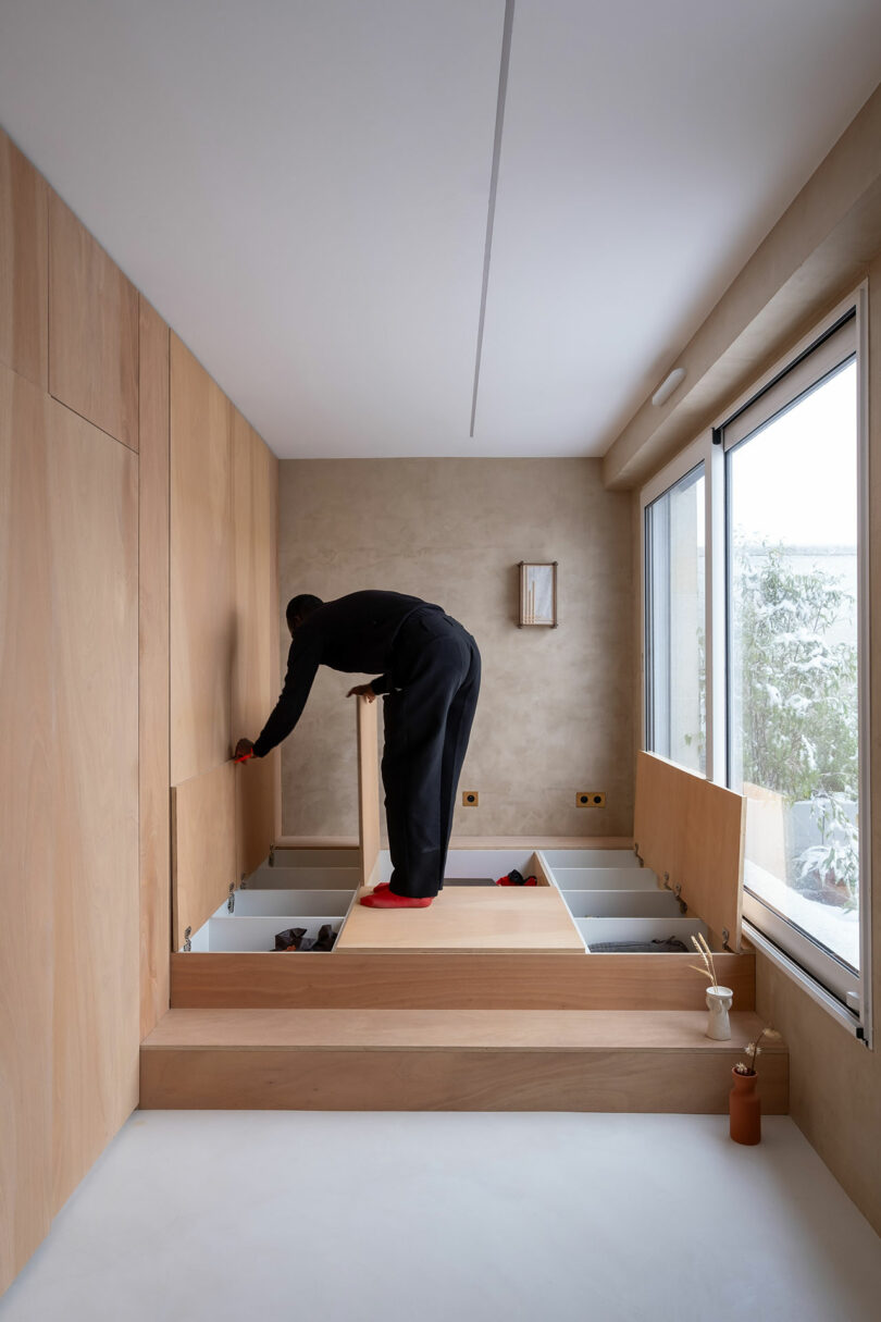 A person opening a wooden lid on a floor platform to reveal built-in storage space.