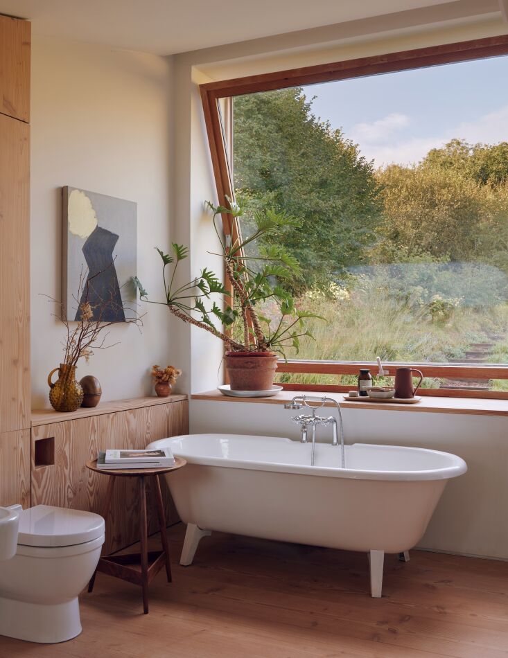 A master bathroom suite with a cast-iron bathtub and large pivot windows looking out over a fruit orchard.
