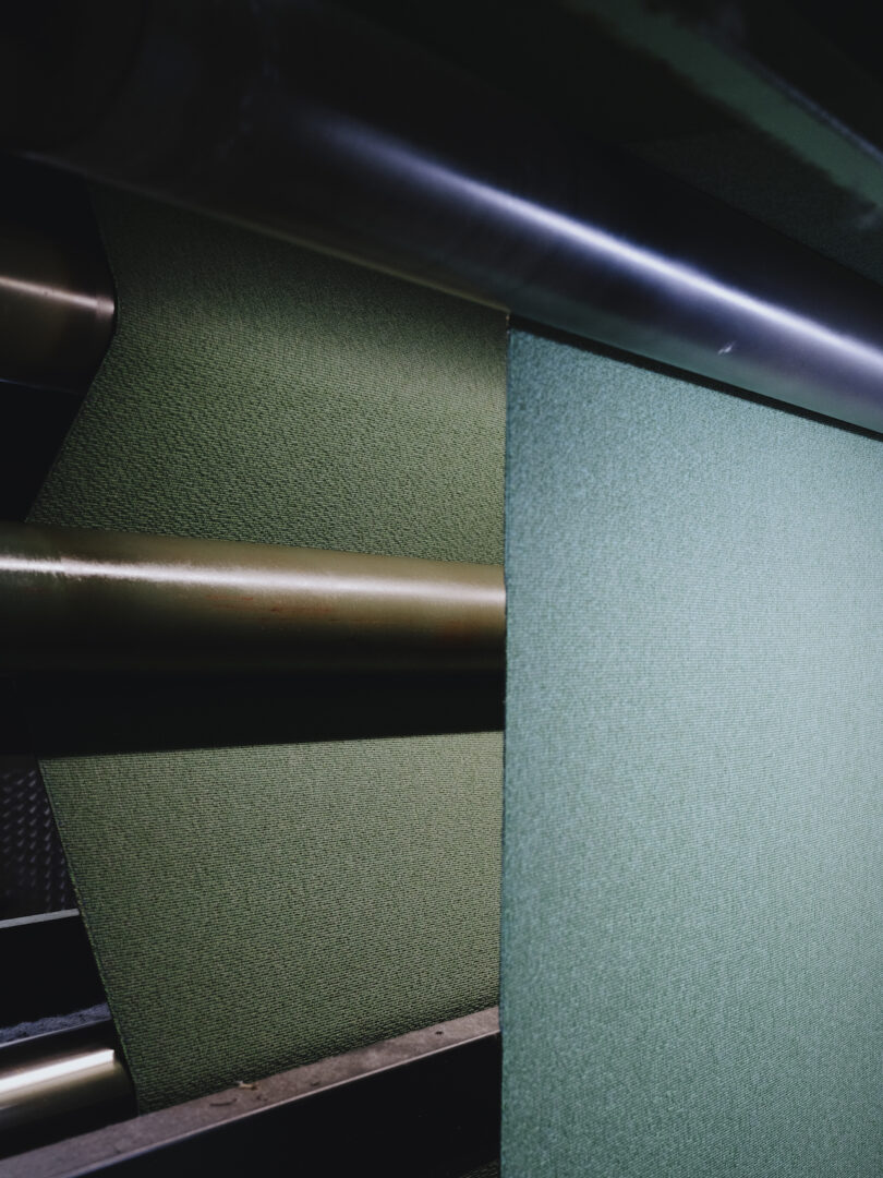 Close-up of green textured fabric being processed through industrial rollers.