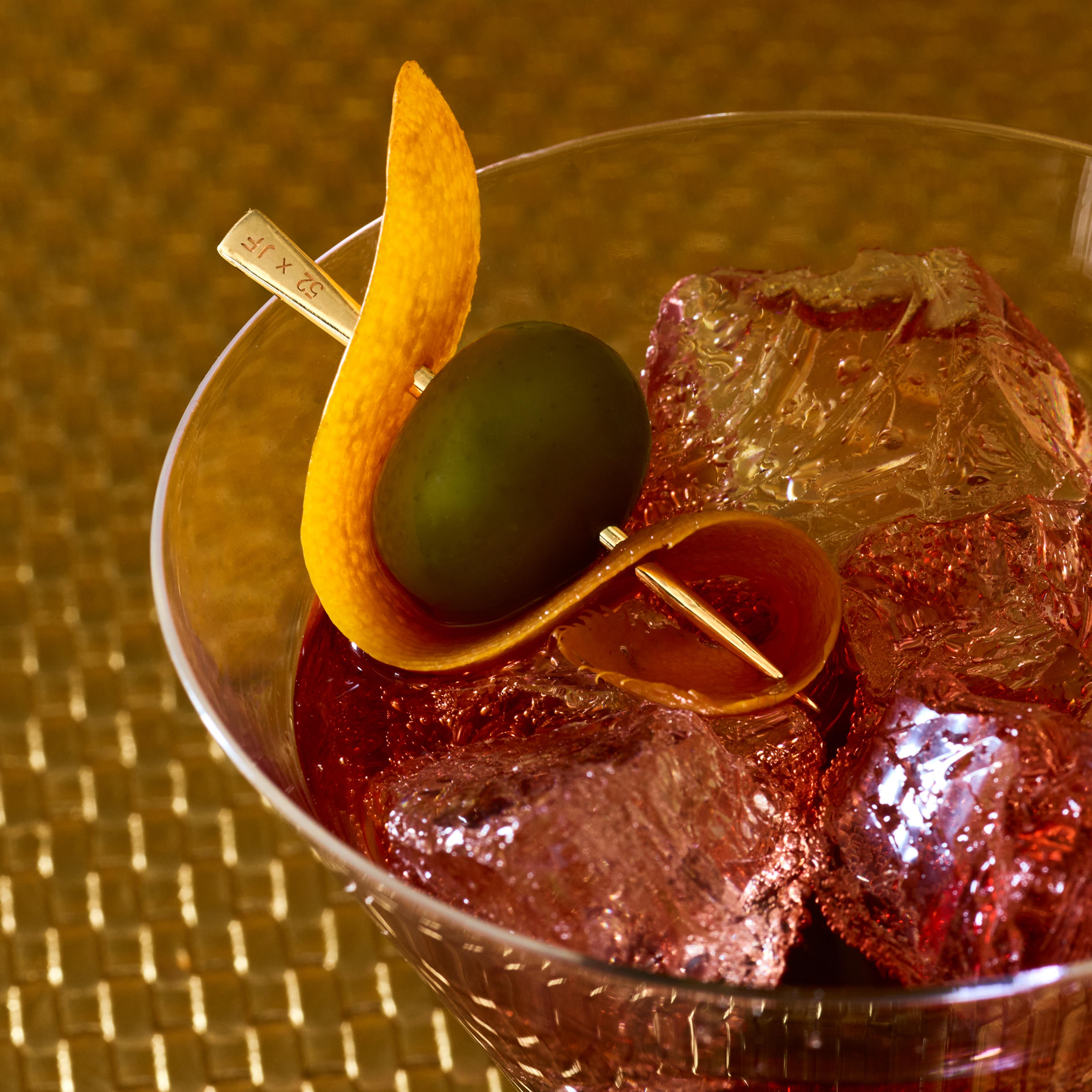 A gold toothpick used as a garnish for a martini with green olives.