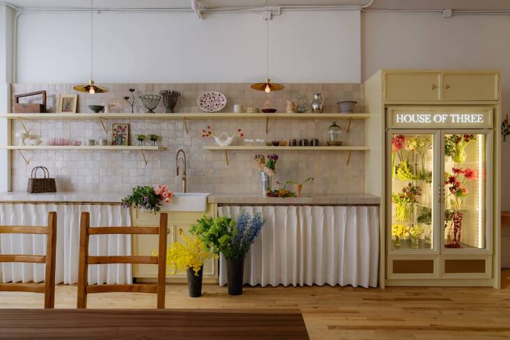 A florist's kitchen featuring a farmhouse sink, brass pendants, and glass flower fridge.
