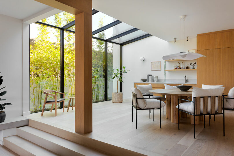 Modern dining area with wooden furniture, floor-to-ceiling windows, and a skylight creating a bright atmosphere.
